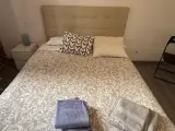 Cama doble vista de frente con toallas azules y beige dobladas y mesilla de noche blanca